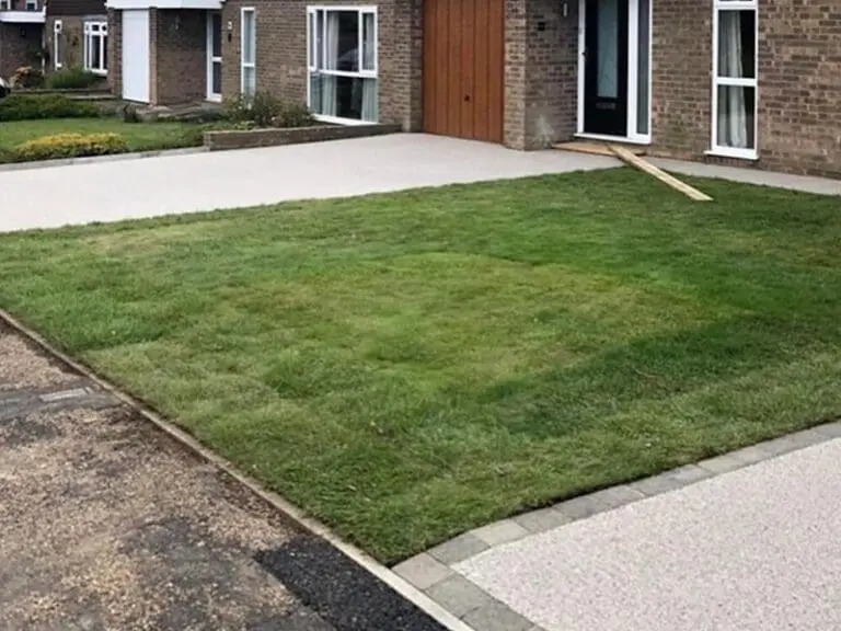 A lawn in front of a house with a clearly visible square patch of grass that is a different shade of green from the rest, suggesting recent repair or new sod.