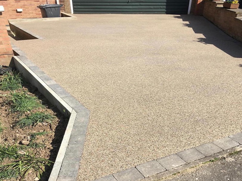 A smooth, newly finished concrete driveway with a raised border and planting bed on one side, leading up to a green garage door.